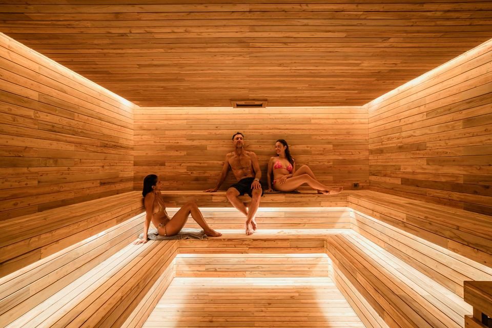 The cedar sauna interior — wide blonde wood, U-shaped bench, light strips at the base of the benches and around the perimeter of the ceiling, a single vent port
