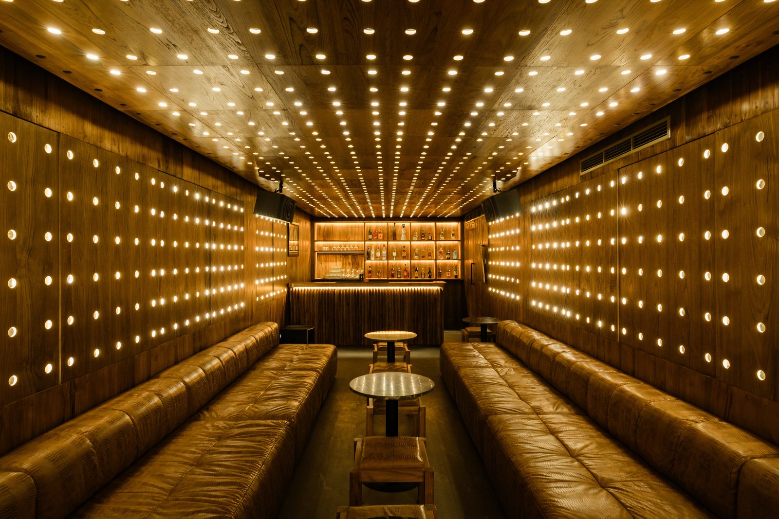 The YLB Bunker karaoke lounge — long tan leather banquettes facing each other, marble-topped low tables, teak panelled walls and ceiling pricked with hundreds of small bulbs in a geometric grid, a backlit bar at the rear