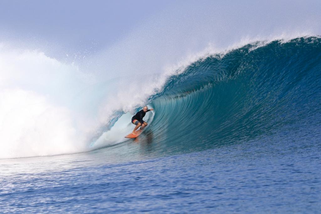 Troy Sinclair inside the barrel of a clean reef wave — deep in the pocket, knees bent, the lip pitching above him, the wave glassy and translucent blue-green