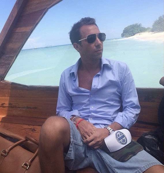 Josh Forrow on a boat in the Indonesian archipelago — light blue shirt, aviators, the white sand and turquoise water of a Bali island beach in the distance