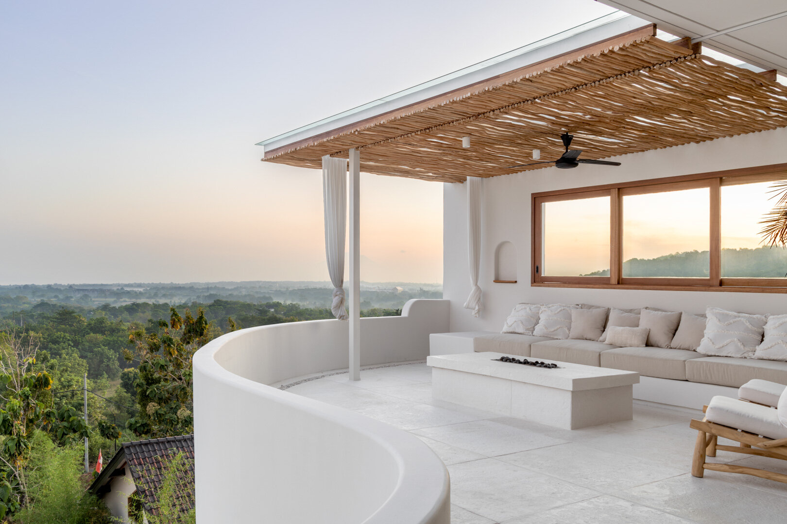 The upper balcony at Villa Zyloh at sunset — curved white plaster walls, woven driftwood ceiling, the fire pit and the long view west over the Bukit