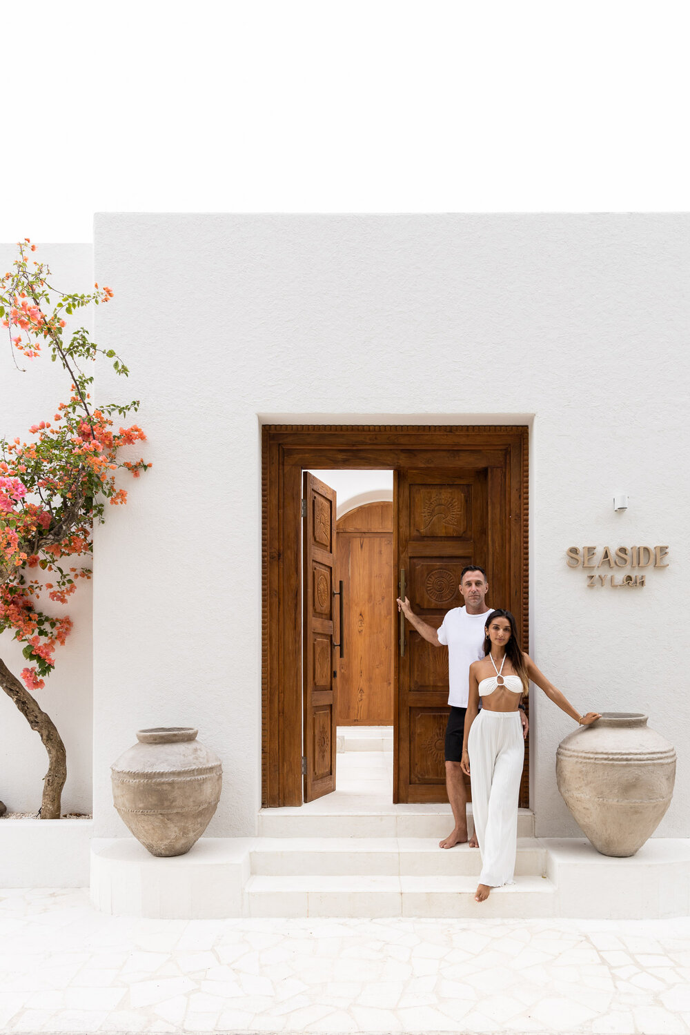 The entrance to Seaside Zyloh — carved teak doors, white stucco, bougainvillea, large terracotta urns at the threshold